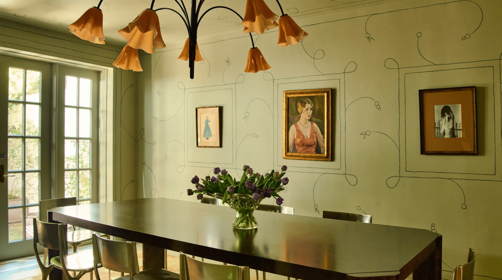 In Courtney Grow’s dining room, a richly grained rectangular wood table is paired with polished chrome chairs, creating a striking contrast to the sculptural chandelier overhead and the custom mural by Alley Bell. Together, these elements bring a sense of balance between structure and spontaneity.